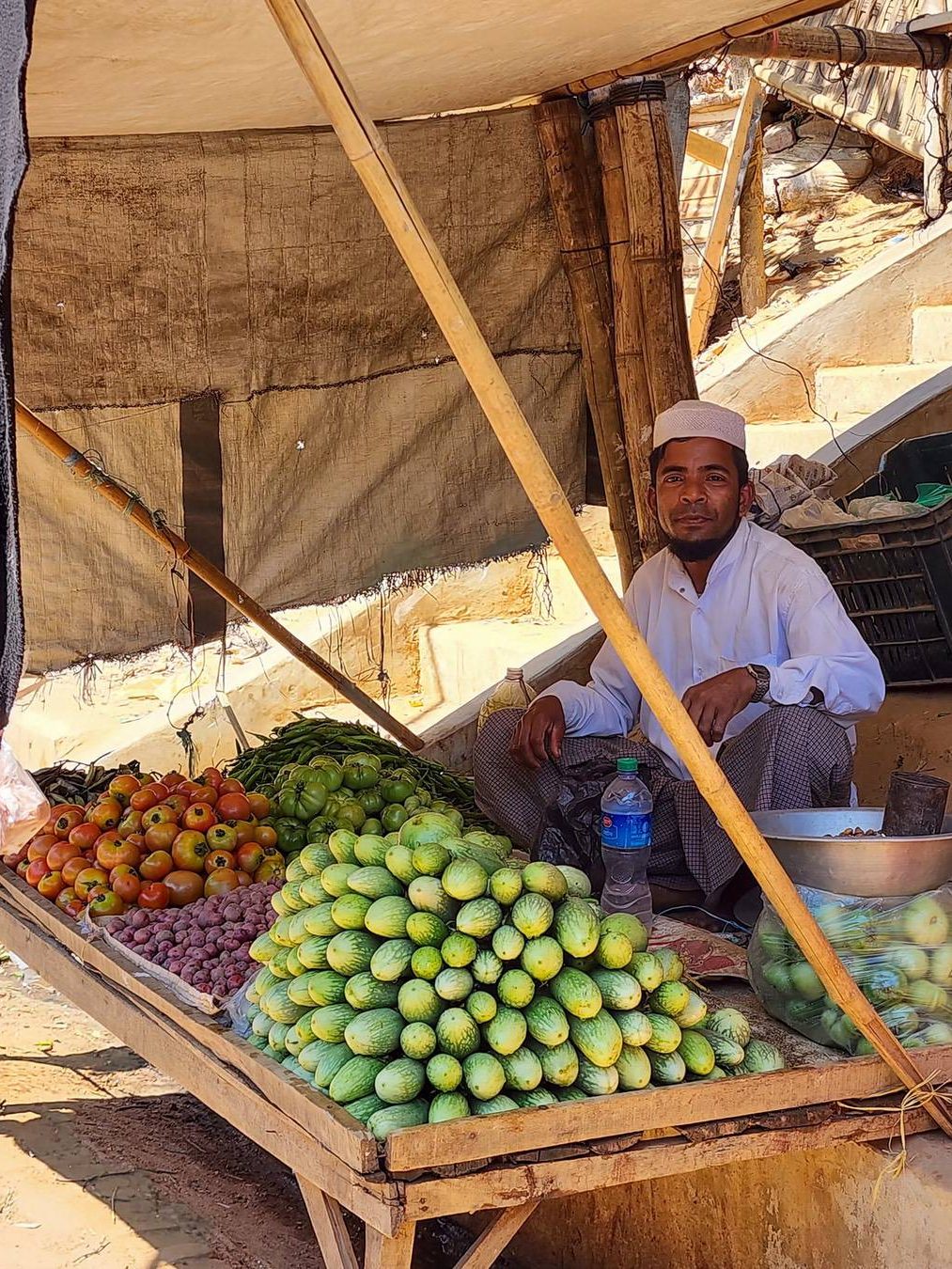 A Rohingya
street vendor – the sole
breadwinner for his family – sells
vegetables in a small stall along the
street in the camp.