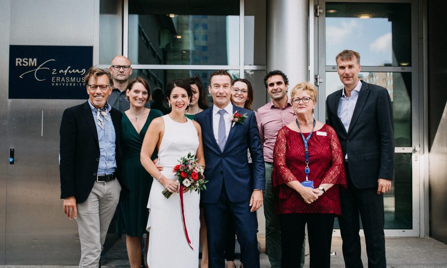 A picture of a married couple standing outside the Bayle Building in their wedding clothes surrounded by RSM staff