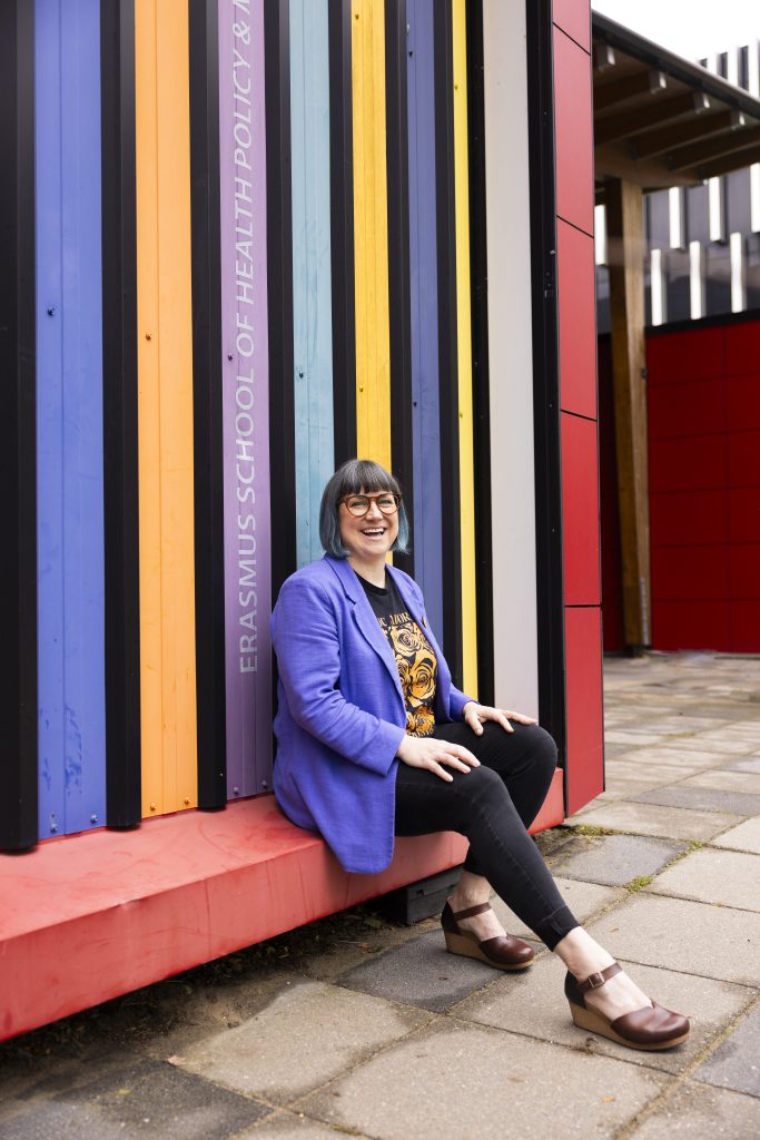 A photograph of Bex Hewett smiling against a very colourful background