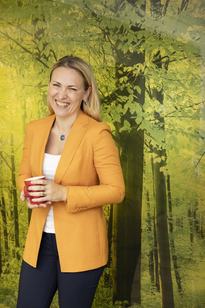 A photograph of Maja Mikielska-Hop laughing amongst a painted backdrop of trees.